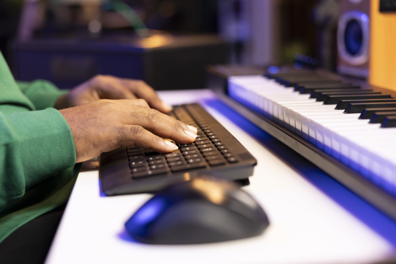 A young producer working on a track at a keyboard and computer workstation